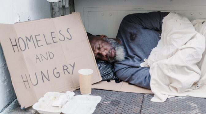 photo of a homeless man sleeping near a cardboard sign